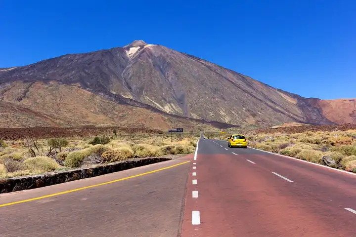 Foutparkeerders in het Teide Nationaal Park -
gele auto rijdt richting Teide op zonnige weg.