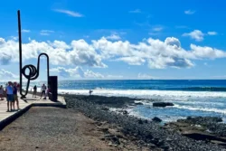 Stranden Tenerife Costa Adeje met kunstwerk en wandelaars onder blauwe lucht.
